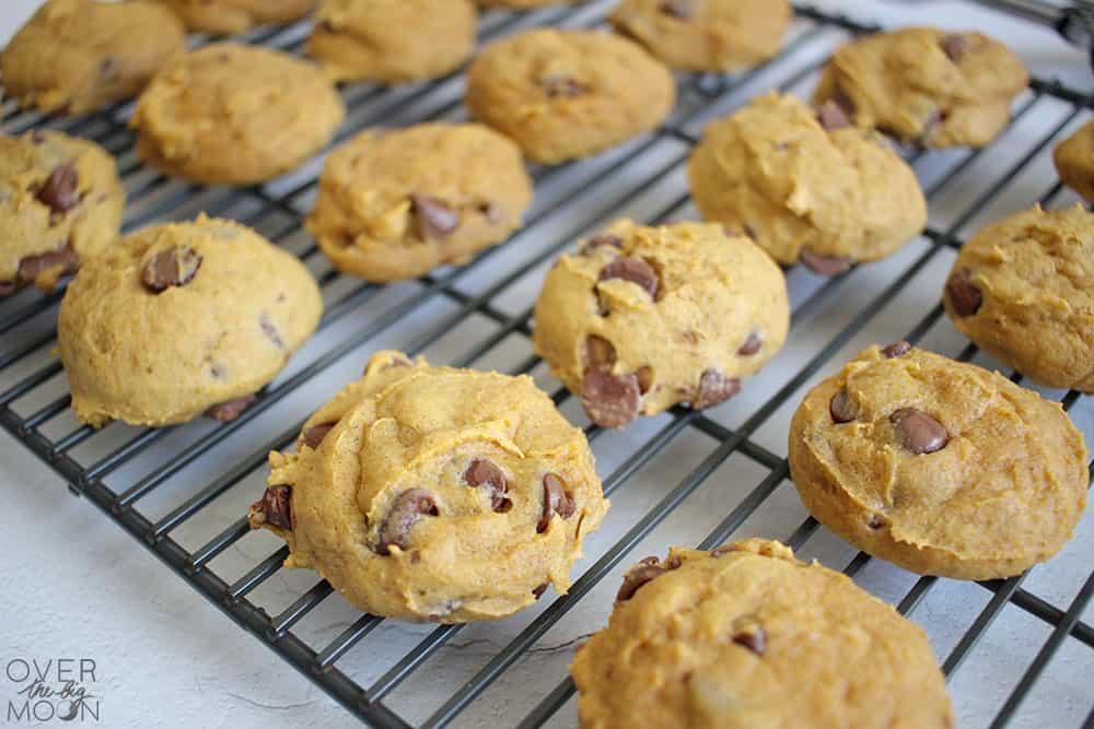 Soft pumpkin chocolate chip cookies cooling on wire racks with visible chocolate chips and a source watermark