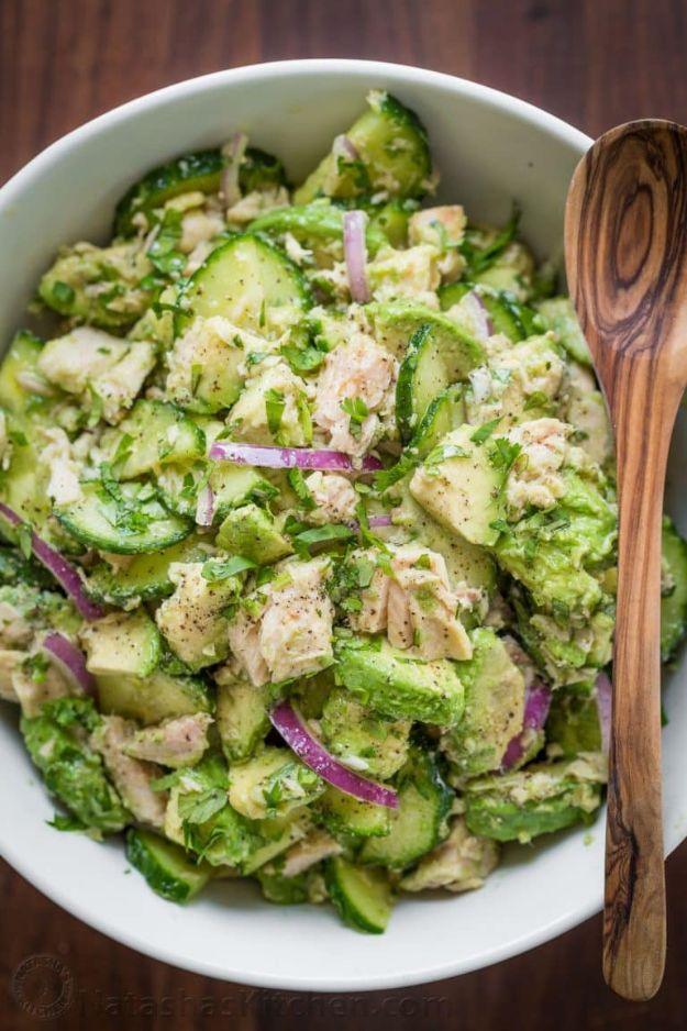 Avocado tuna salad with sliced cucumber, red onion and cilantro in a large white bowl with a wooden spoon