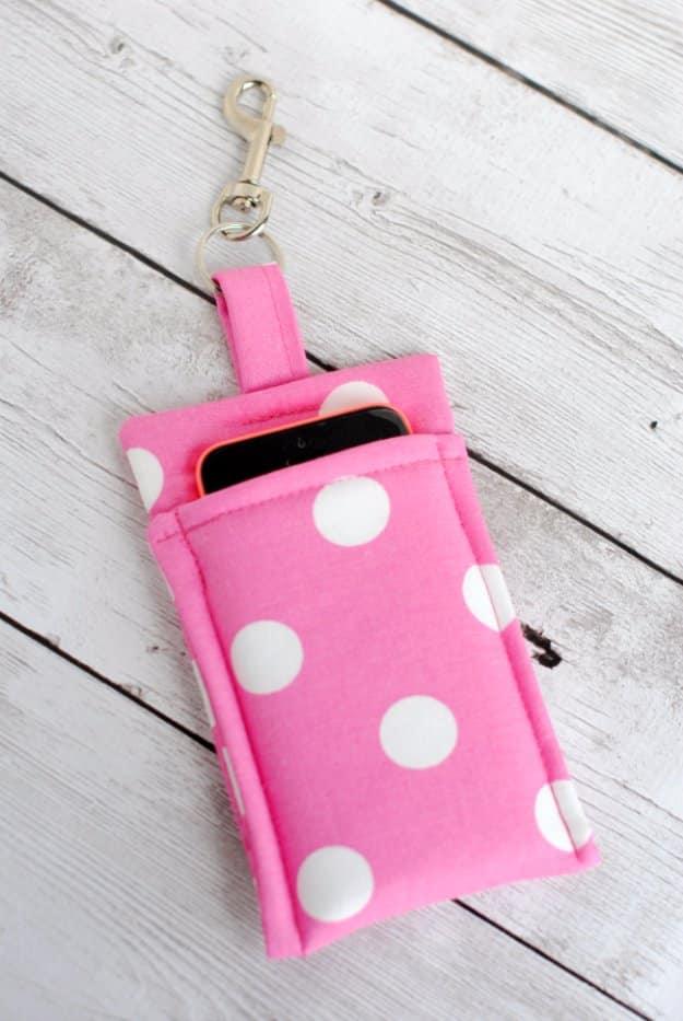 Pink and white polka dot fabric phone wallet with a gold swivel clasp on a strap, holding a phone, on white boards