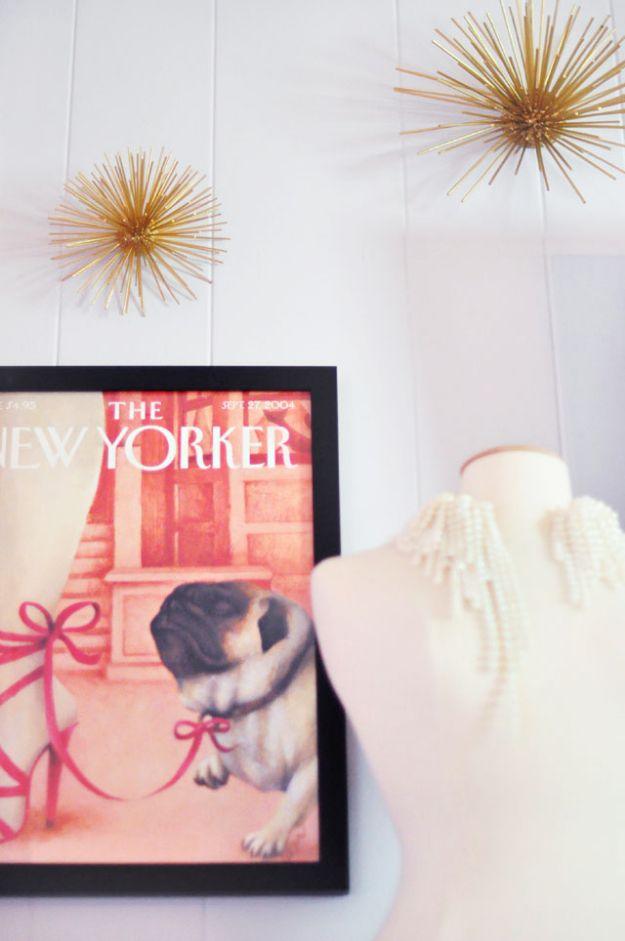 Two gold spiked sea urchin starburst wall sculptures on white paneling above a framed magazine print and pearl necklaces