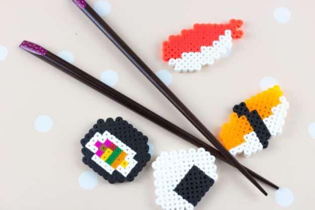 Perler bead sushi magnets, four fused bead sushi pieces in black white red and orange beside black chopsticks