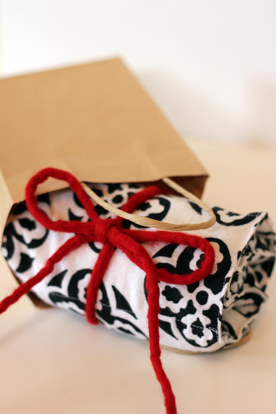 A black and white flannel rice heating pad rolled up and tied with a thick red yarn bow, held in two hands