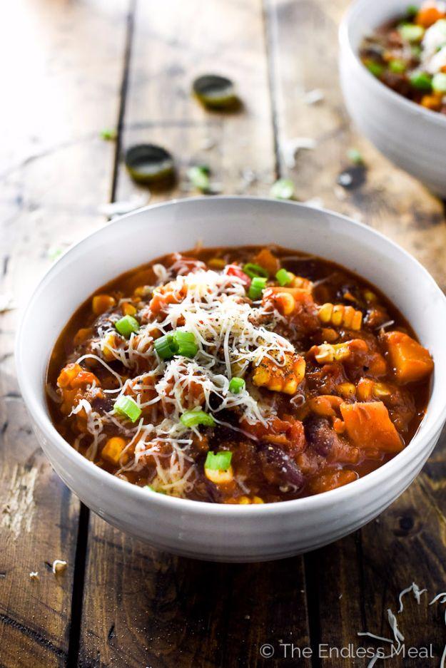 Chipotle bourbon pumpkin chili in a white bowl with corn, squash cubes, grated cheese and sliced green onion