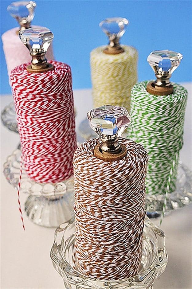 Four glass candleholders holding spools of red, green and brown baker's twine on dowels topped with glass knobs