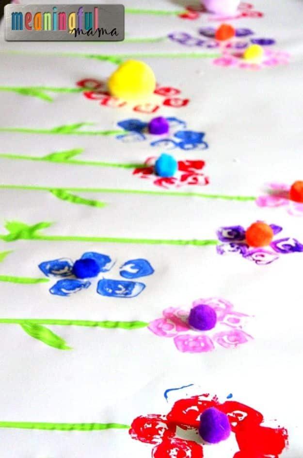 Painted flower prints stamped with egg carton cups along a long roll of craft paper with pom pom centers