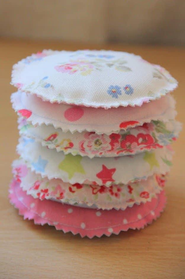 Seven round fabric pocket warmers in pastel floral and dot prints stacked on a wooden table with pinked scalloped edges