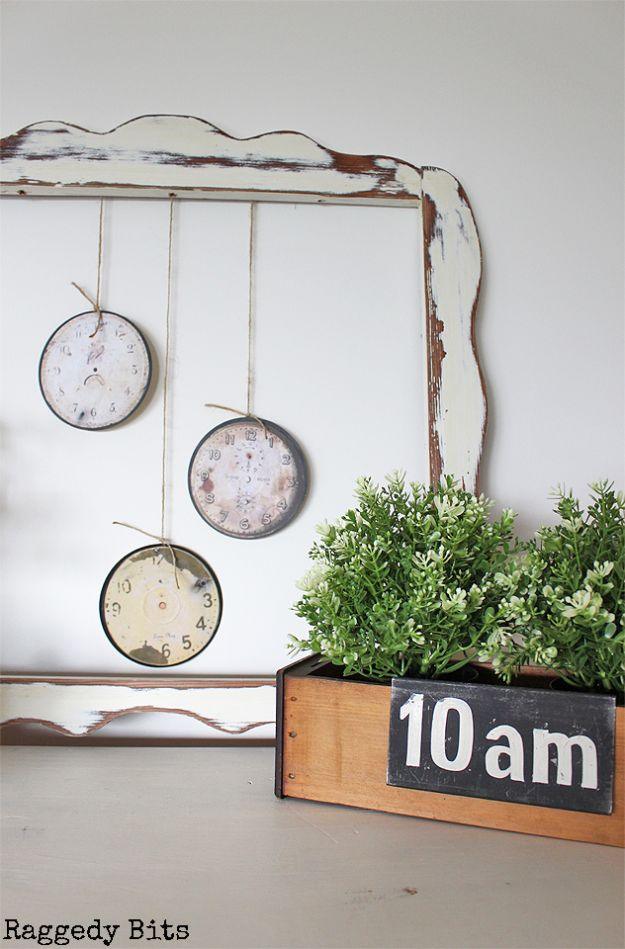 Three clock faces made from old CDs hanging on twine inside a chippy white frame above a wooden planter box