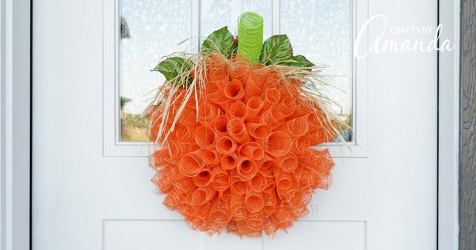 Orange deco mesh pumpkin wreath with a green stem hanging on a front door, a bright fall wreath for autumn
