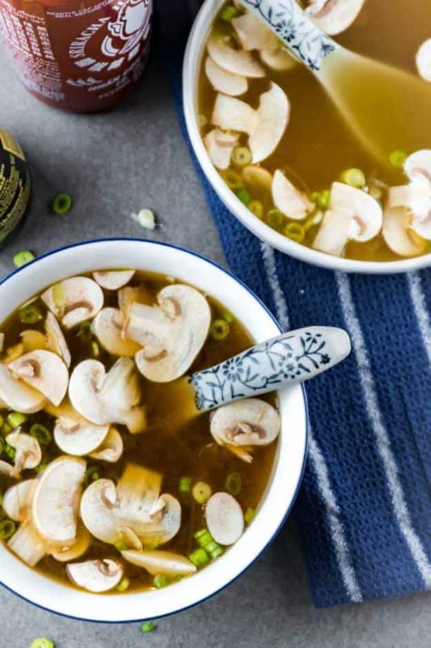 Japanese clear onion soup in a white bowl with thin sliced mushrooms and scallions floating in clear broth