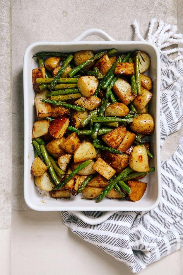 White baking dish of balsamic roasted new potatoes and green asparagus pieces on a striped kitchen towel