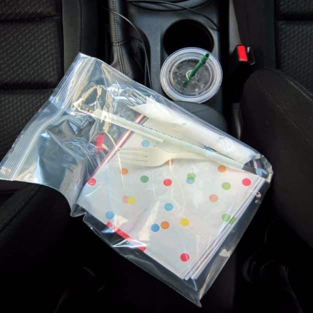 A polka dot zip top bag of napkins and plastic forks resting on a car center console beside a cup in the holder
