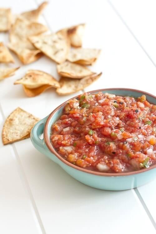 Restaurant style salsa in a bowl with fire roasted tomatoes and cilantro beside a pile of tortilla chips