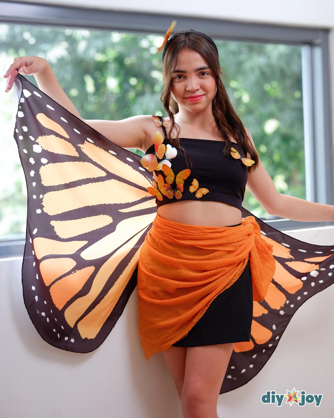 Butterfly Costume - woman by a window holding out one orange and black monarch wing over a crop top and sarong