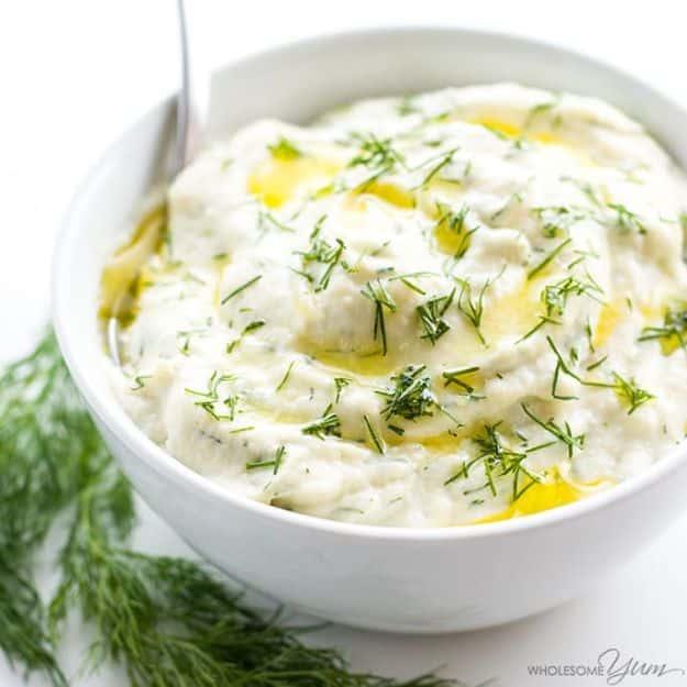 Creamy mashed cauliflower in a white bowl scattered with fresh dill and drizzled with green olive oil