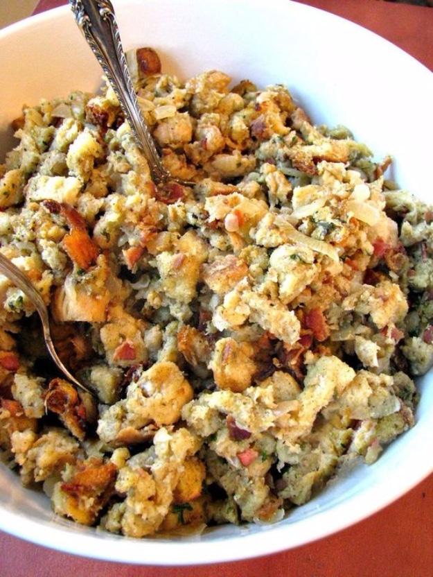 Chunky bacon, onion and sage stuffing in a white bowl with ornate serving spoons for a Thanksgiving side dish