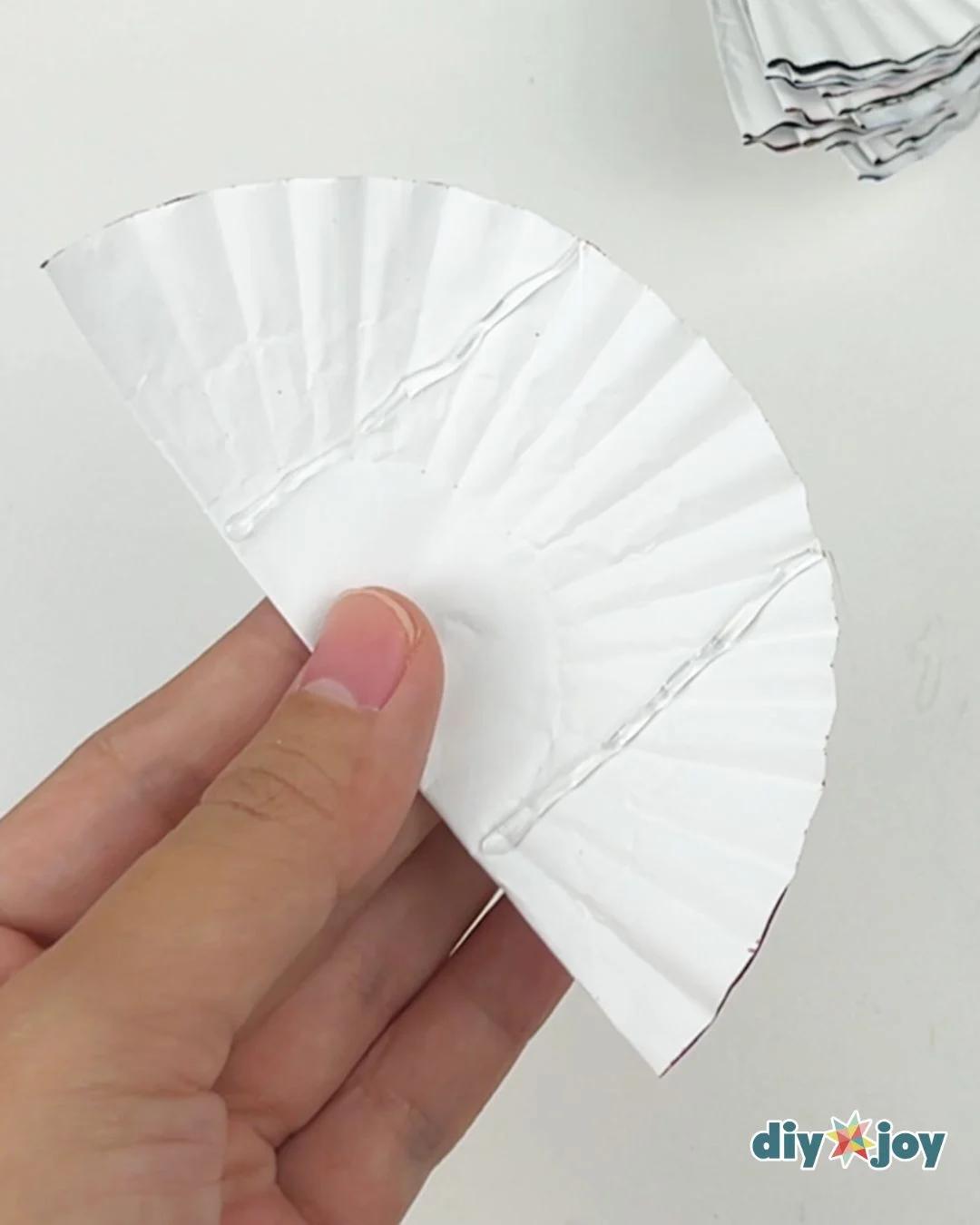 DIY Paper Crafts - a white cupcake liner folded into a half circle fan held between a thumb and finger