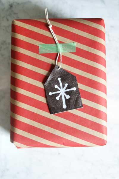 A red and kraft striped wrapped parcel with a dark leather gift tag hand painted with a white snowflake