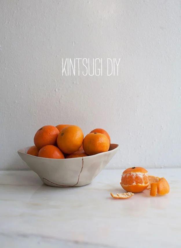 White ceramic bowl with a gold repaired crack down one side, filled with clementines on a white marble counter