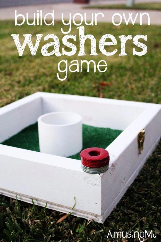 DIY washers game box with a white painted frame, green turf base and a white PVC cup set in the backyard grass