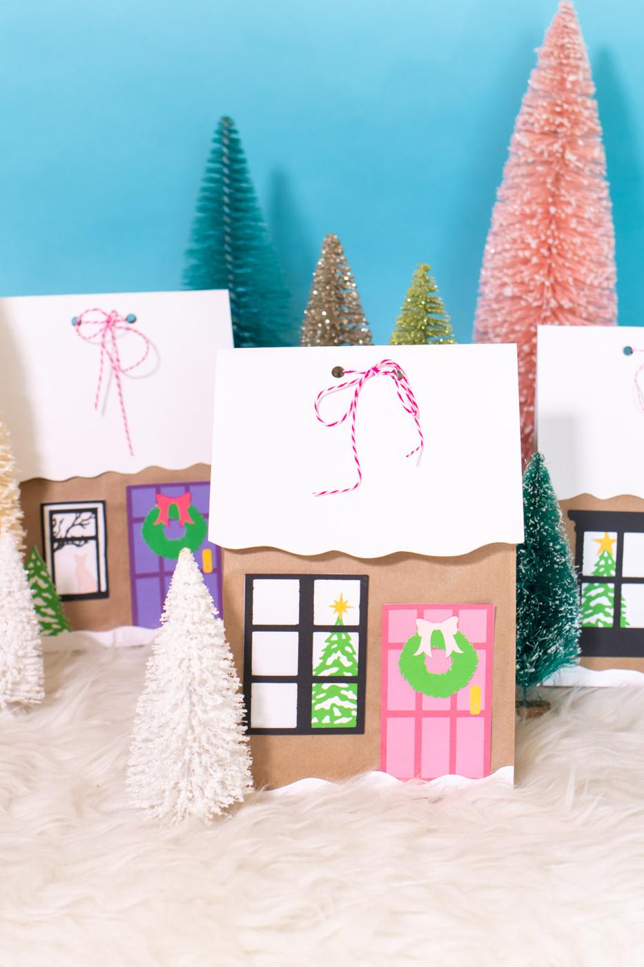 Brown paper lunch bags decorated as gingerbread houses with snowy white roofs, pink doors and paper wreaths