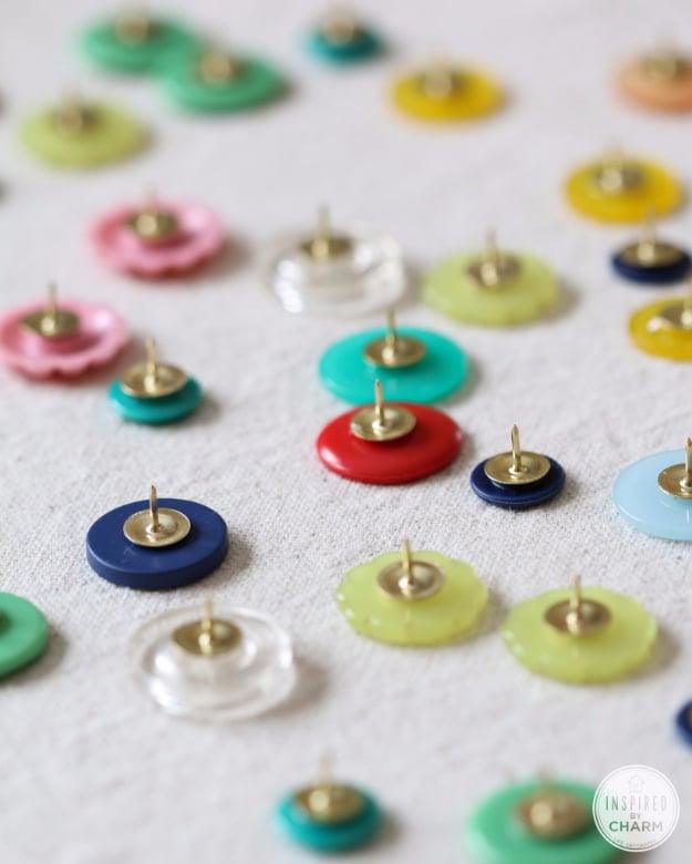DIY button thumb tacks, dozens of small coloured buttons glued to the heads of brass thumb tacks on a pale surface