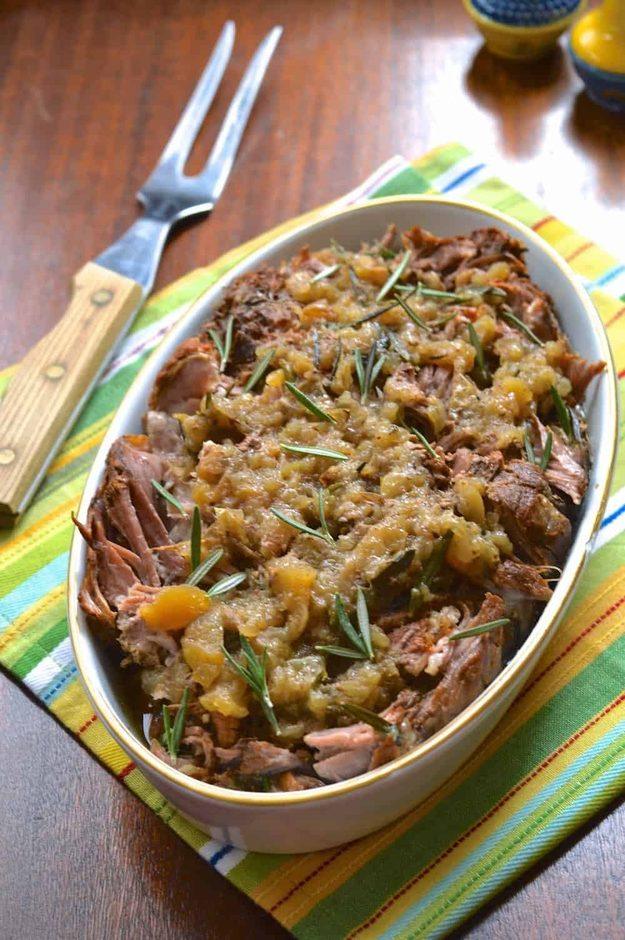 Cooked pork roast under chunky apples and rosemary in a white oval dish beside a cloth and carving fork