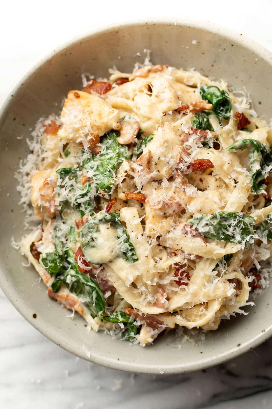 Chicken bacon spinach pasta in a speckled bowl, creamy pasta with wilted spinach and crisp bacon pieces