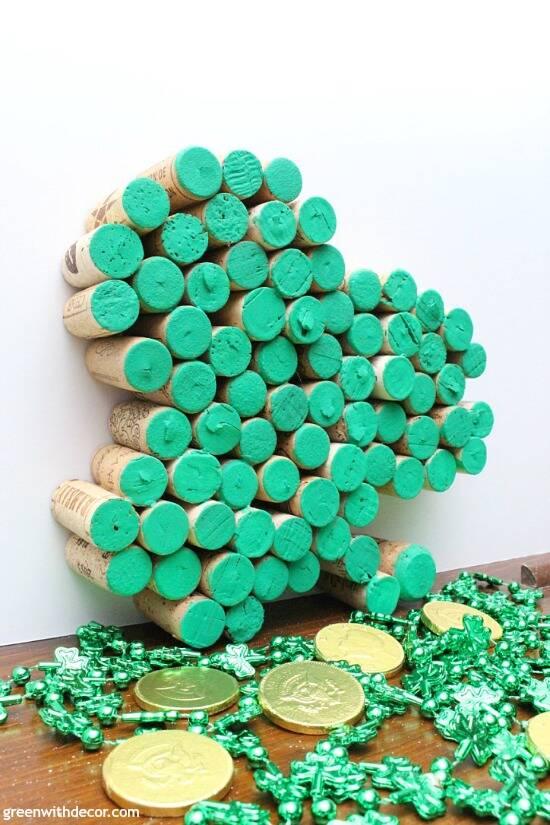 St. Patrick's Day decor, a shamrock made from wine corks with the cork tops painted green, propped against a wall beside gold coins