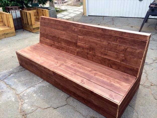 Heavy dark brown stained pallet sofa with a wide seat and tall solid plank back on a cracked concrete driveway