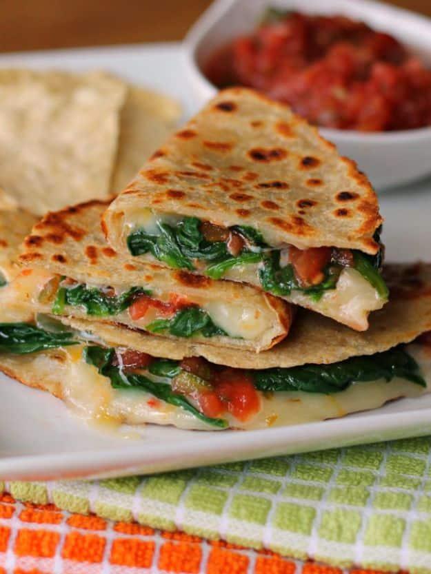 Stacked wedges of spicy spinach quesadilla with melted cheese and a bowl of red salsa set behind them