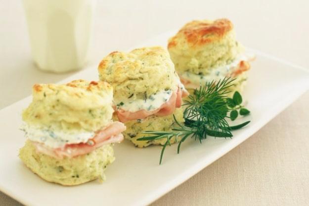 Herb and cheese scones split and filled with chive cream, stacked on a plate with fresh chives scattered