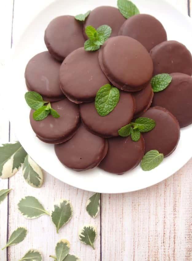 Gluten free thin mint cookies coated in dark chocolate and stacked on parchment paper, a vegan copycat