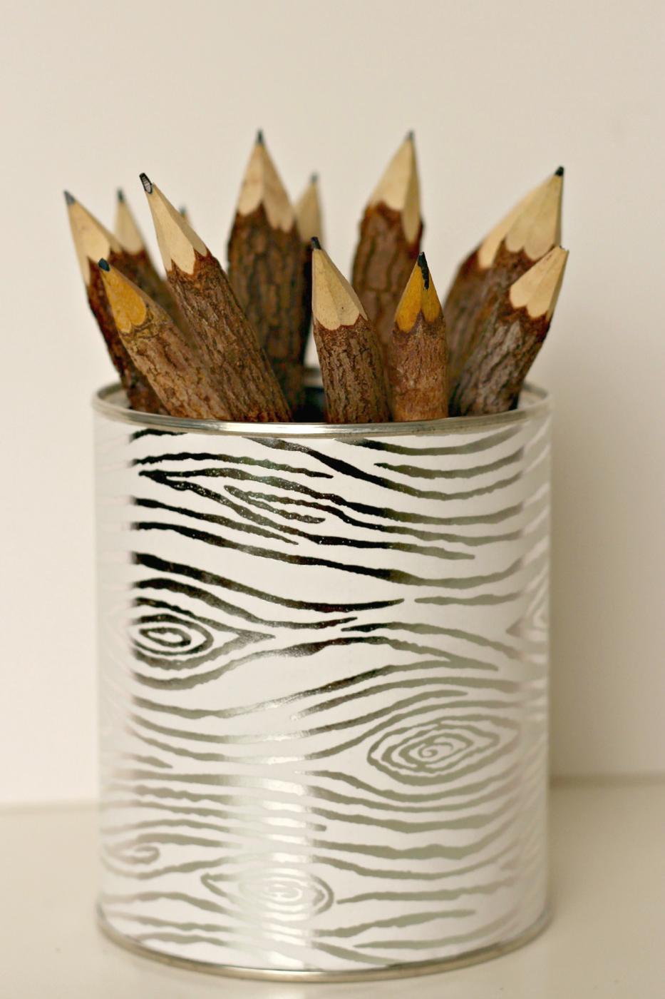 Tall tin can wrapped in silver and white wood grain paper holding a bundle of rustic twig pencils on a white surface