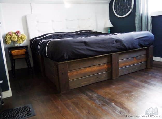 Photograph of a tall dark stained plank sided platform bed with black bedding and a white tufted headboard