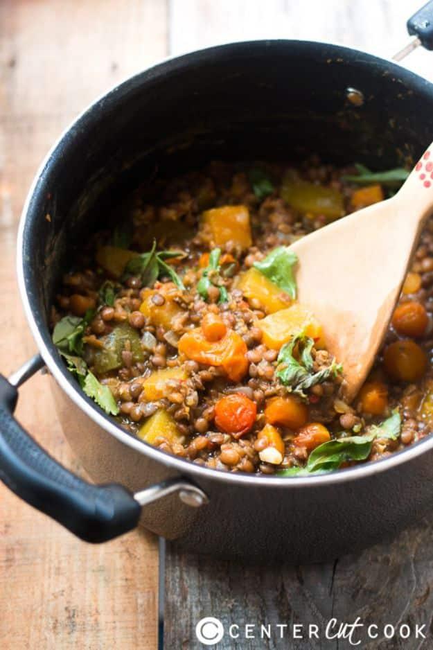 Black pot of lentil and pumpkin stew with carrots, celery and cilantro, a wooden spoon resting inside