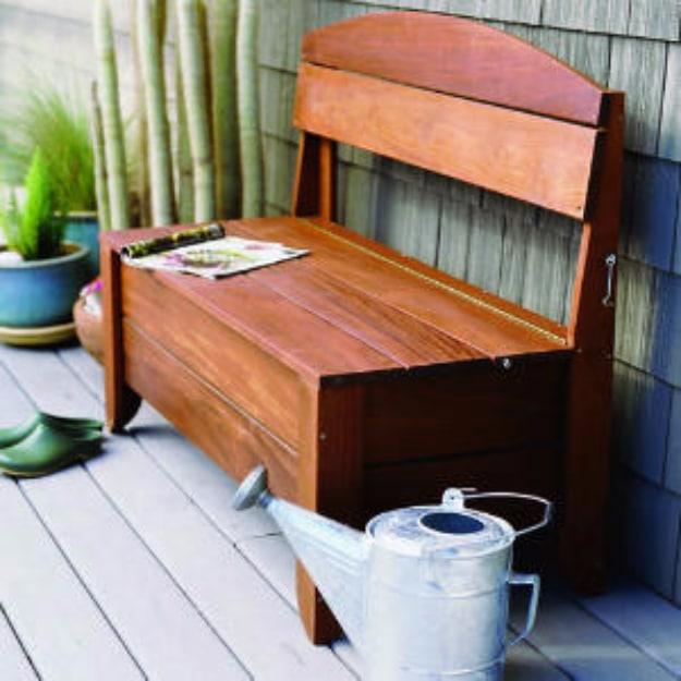 DIY curb appeal storage bench in stained wood with the hinged lid propped open on a gray deck beside a watering can