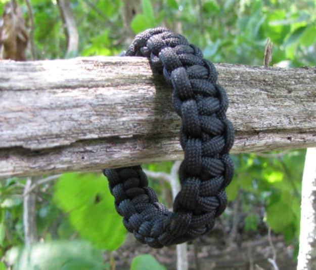 Plain black one color cobra weave paracord bracelet hanging on a bare branch surrounded by green leaves
