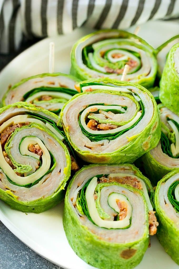 Turkey roll ups sliced into pinwheels on a white plate showing green spinach tortilla, turkey and avocado