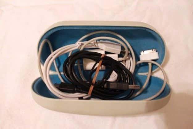 Old hard sunglasses case reused to store loose charging cords, white and black cables coiled inside the blue lining