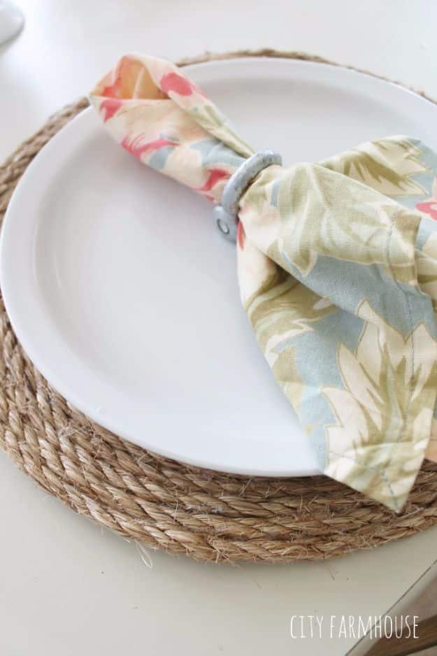 Four round placemats of coiled jute rope sit on a pale wood dining table, each topped with a white stoneware plate