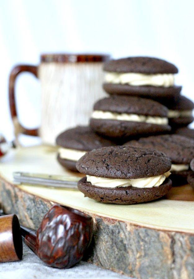 Chocolate espresso whoopie pies stacked with thick white filling on a wood slab beside a striped mug