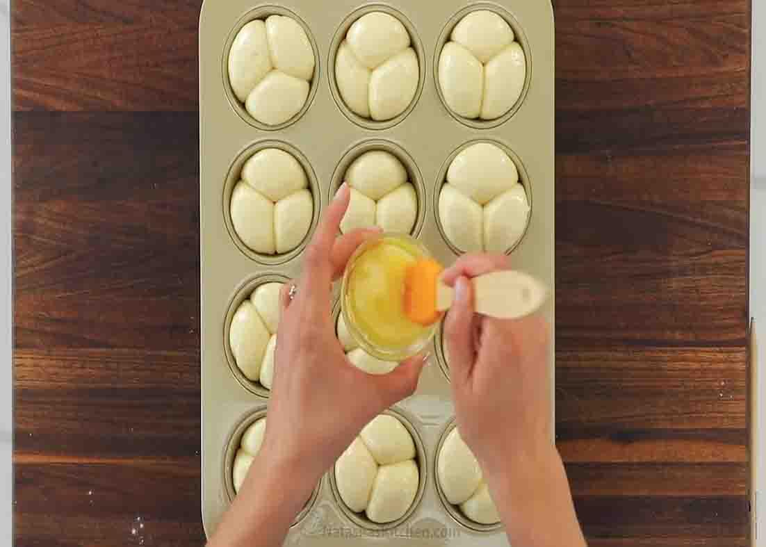 Brushing the tops of the cloverleaf rolls with some butter