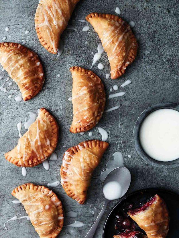 Blueberry hand pies fried golden with crimped edges on a dark surface beside a small bowl of lemon glaze