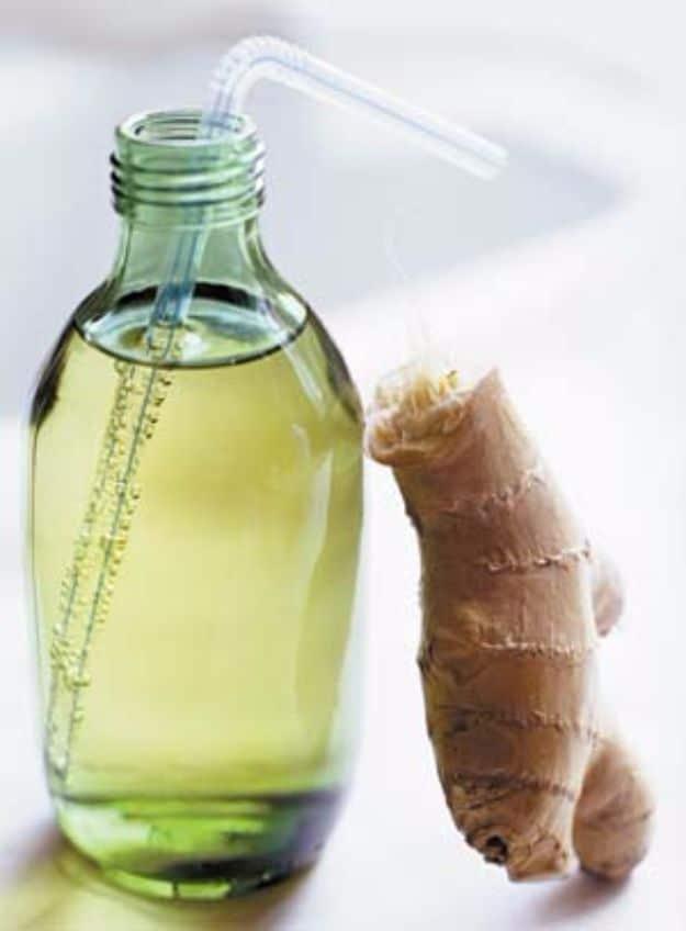 Homemade ginger ale in a bottle and a glass with ice, fresh ginger root and citrus on the counter ready to pour