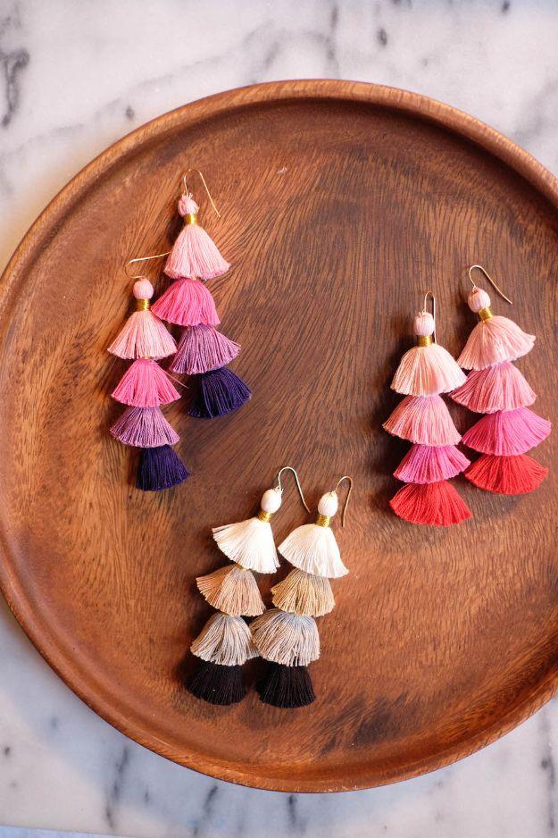 DIY multicolor tassel earrings, three stacked pairs in pink, coral and cream on a round wooden plate on marble