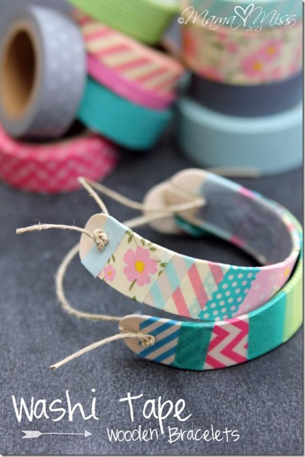 DIY washi tape wooden bracelets, two curved craft stick bracelets in pastel washi tape beside washi rolls on slate