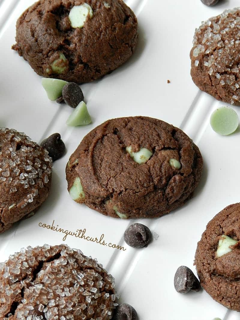 Dark chocolate peppermint cookies studded with green mint chips, some rolled in sparkling sugar, on a white plate