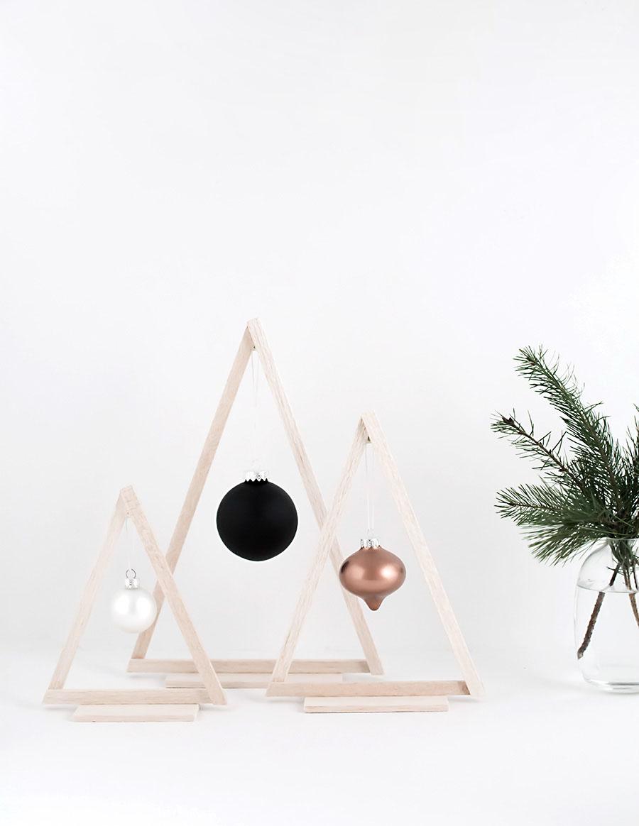 Three open balsa wood triangle trees on flat bases, each holding one ornament in white, matte black or copper