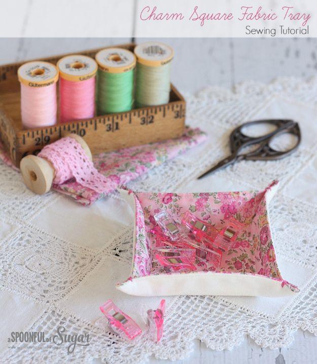 Charm square fabric tray in a pink floral lawn holding sewing clips, on lace beside thread spools and scissors