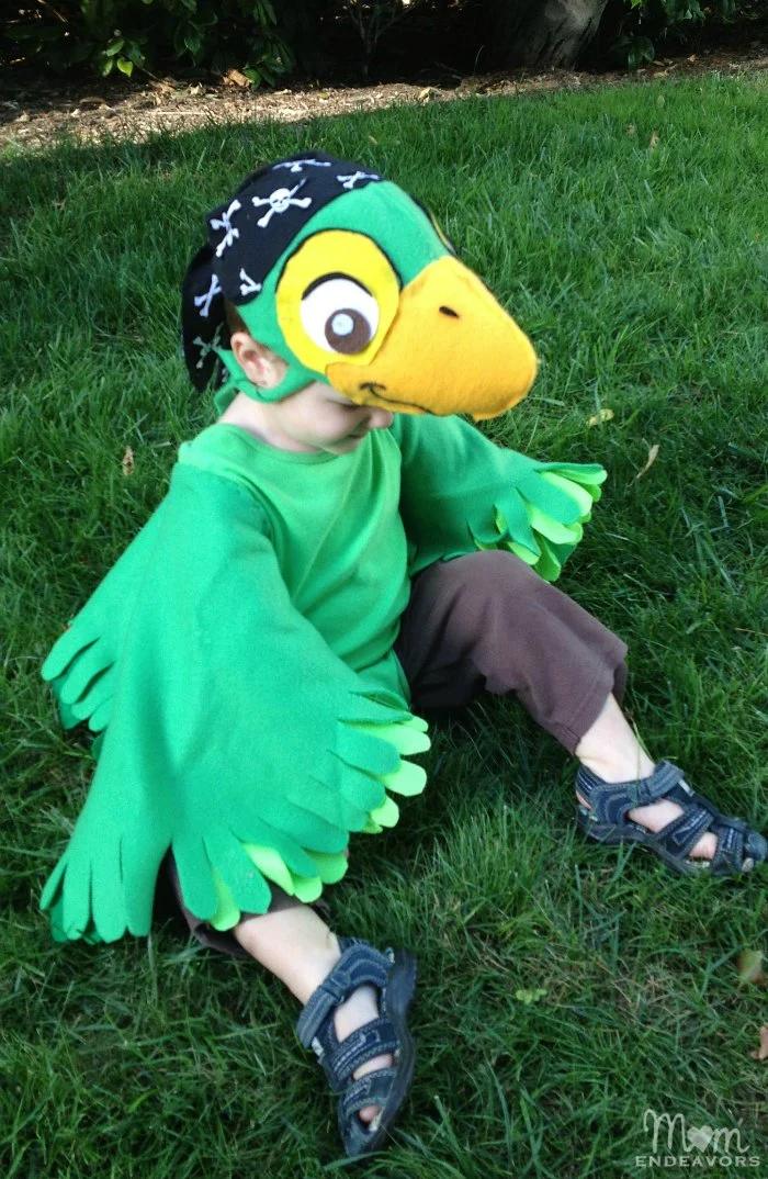 Child wearing a Skully parrot costume with green fleece wings, layered felt feathers, a bright tail and matching cap